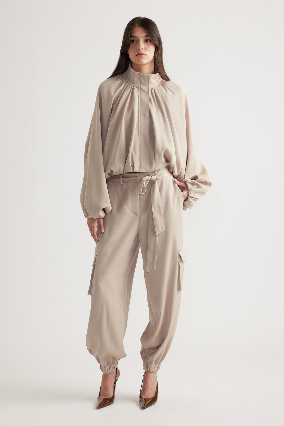 Woman wearing a relaxed biscuit-colored satin bubble jacket with matching cargo-style pants and pointed brown heels