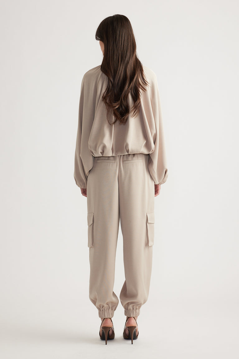 Woman wearing beige relaxed-fit cargo pants and a loose satin bubble jacket paired with black heeled sandals, back view