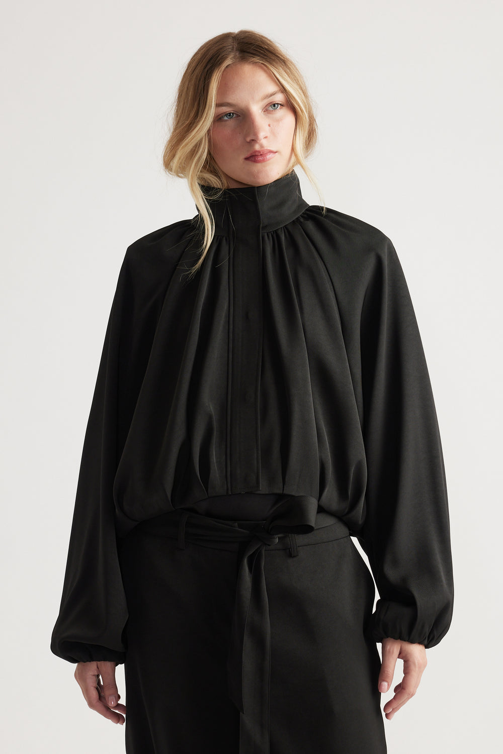 Woman wearing a loose-fitting black satin jacket with high collar and billowing sleeves styled with matching trousers