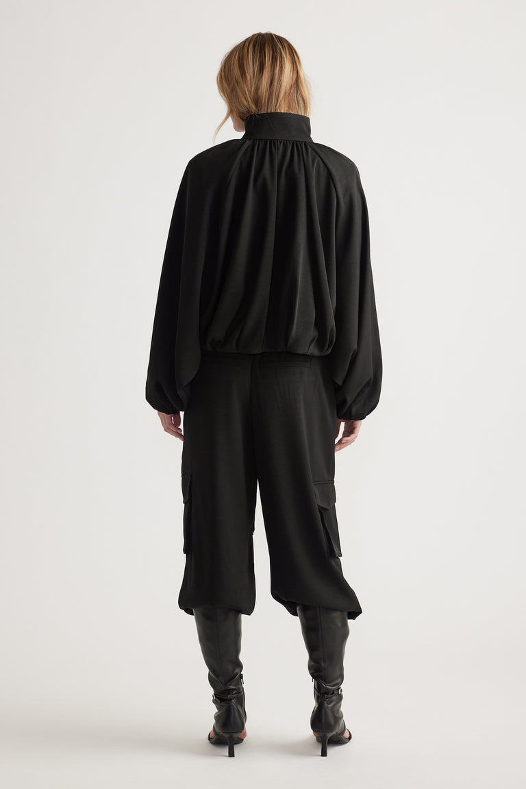 Woman seen from behind wearing a loose black satin bubble jacket paired with cropped wide-leg pants and high black boots