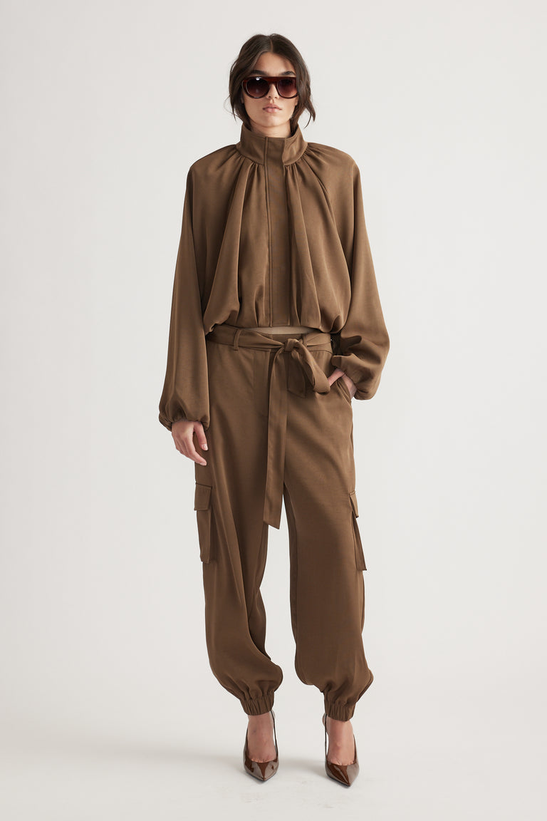 Woman in bronze satin bubble jacket and matching belted cargo pants, styled with sunglasses and heels for a polished look