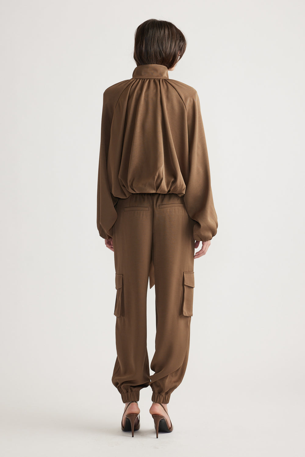 Back view of relaxed-fit bronze satin jacket and matching cargo pants paired with classic black heels