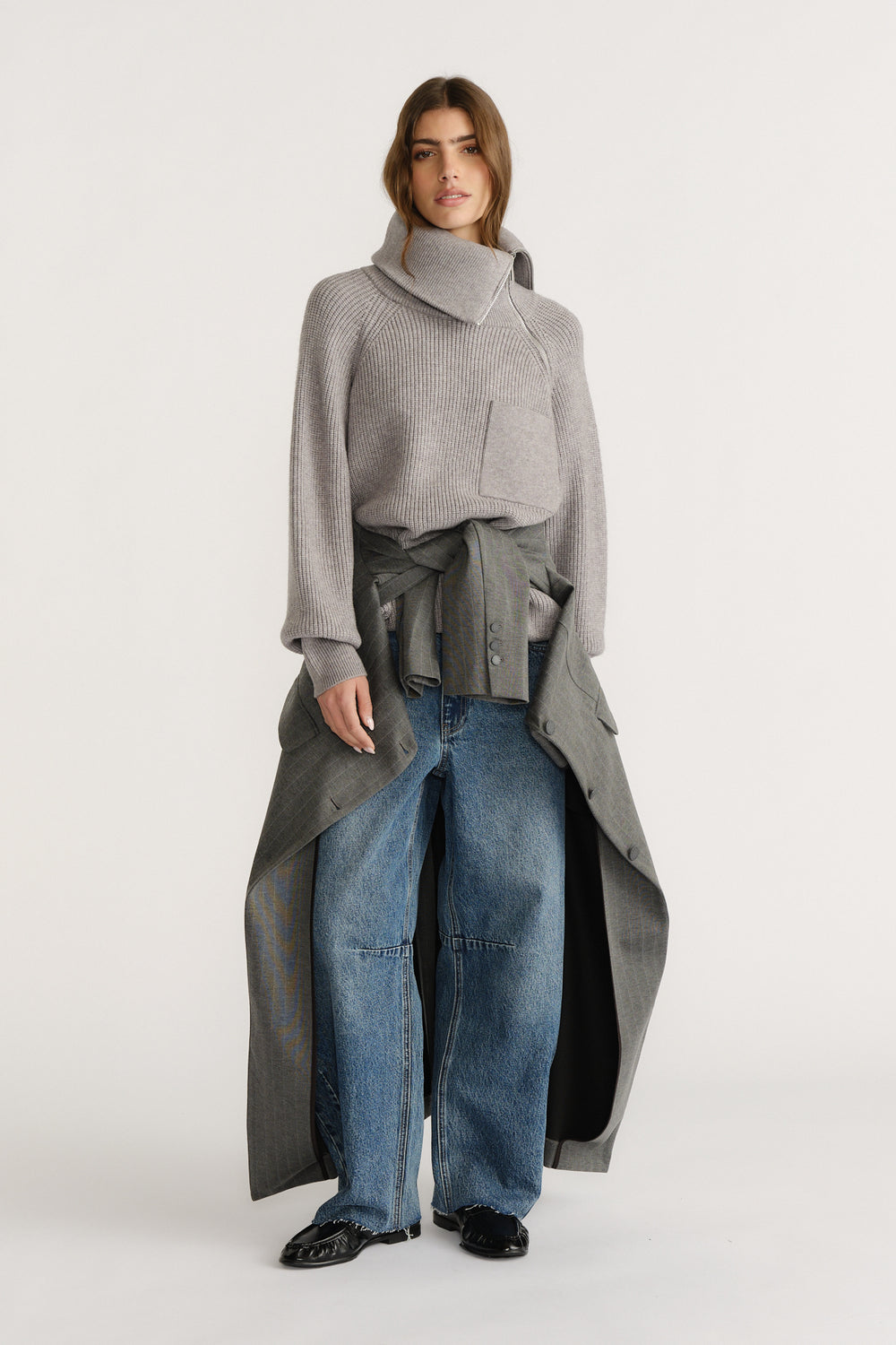 Woman wearing a grey high-neck knit jumper styled with wide-leg denim jeans and a grey coat tied at the waist