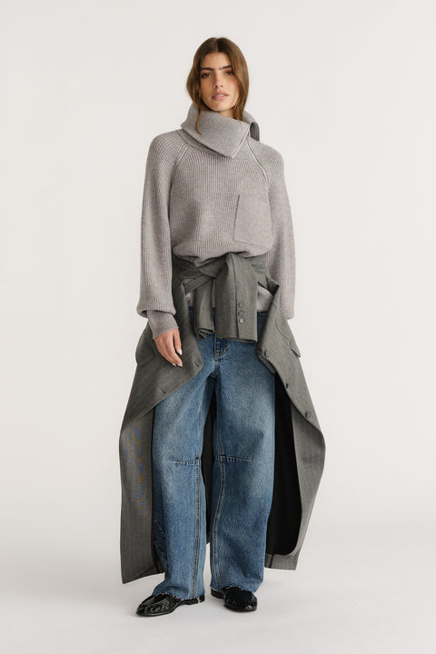 Woman wearing a grey high-neck knit jumper styled with wide-leg denim jeans and a grey coat tied at the waist