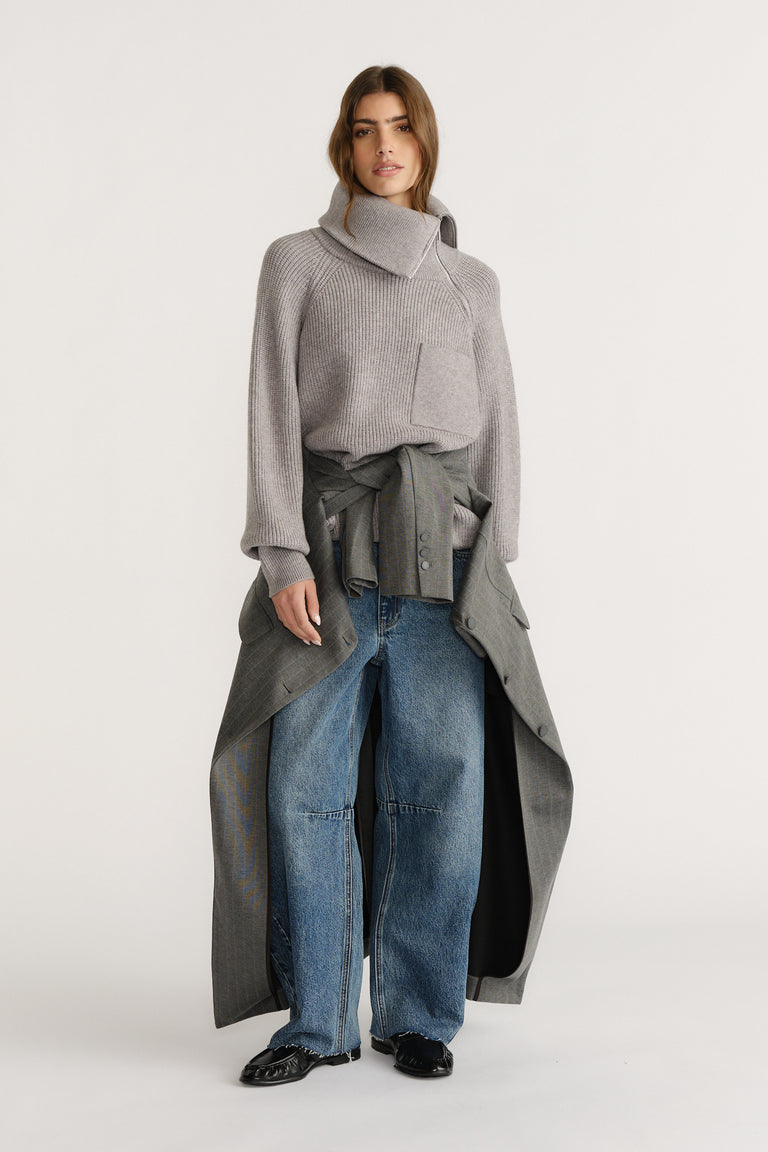 Woman wearing a grey high-neck knit jumper styled with wide-leg denim jeans and a grey coat tied at the waist