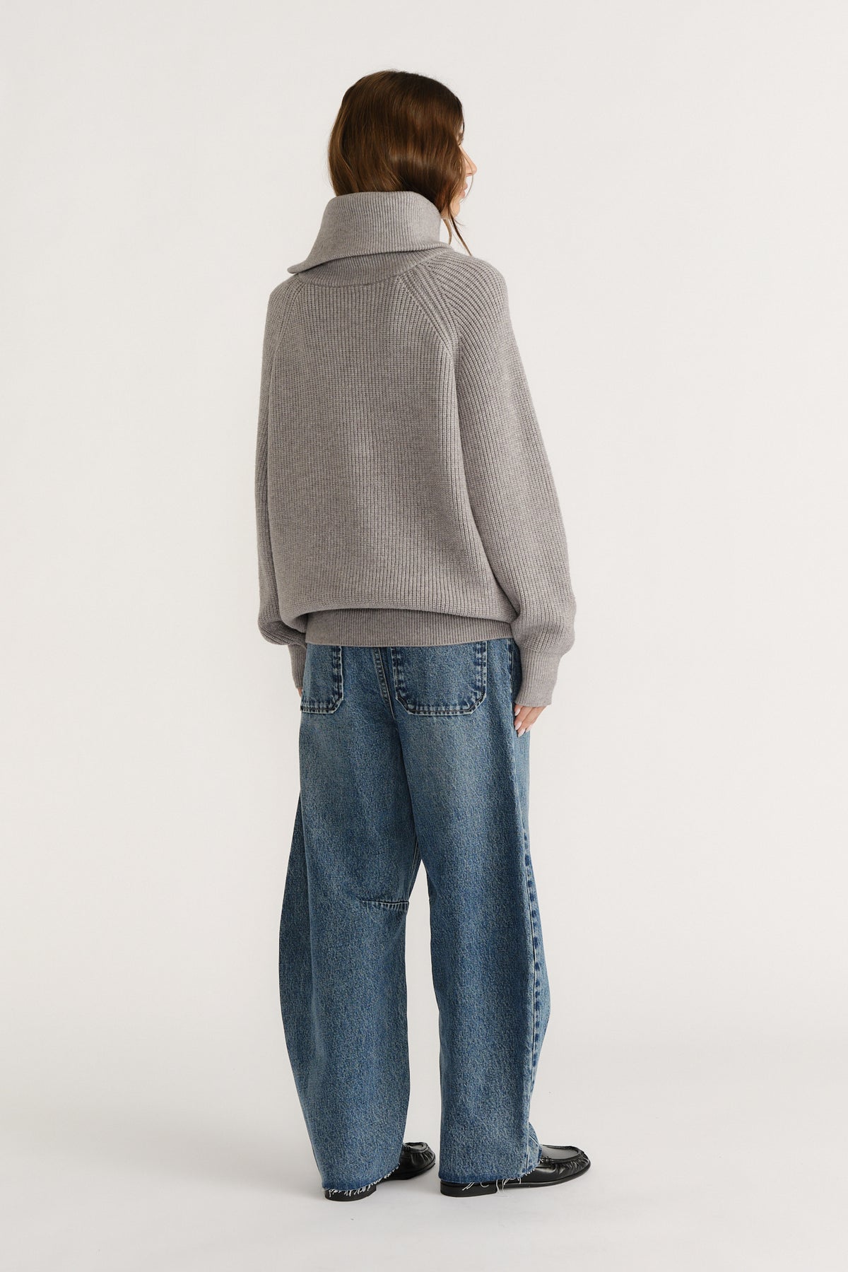 Woman wearing a cozy grey high-neck knit jumper paired with relaxed wide-leg denim jeans and black shoes, back view