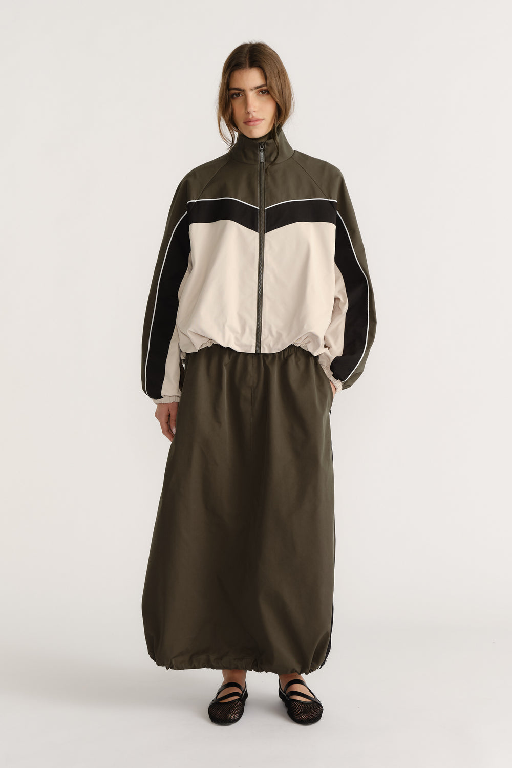 Front view of woman wearing oversized khaki and cream windbreaker with contrast panels and long olive skirt