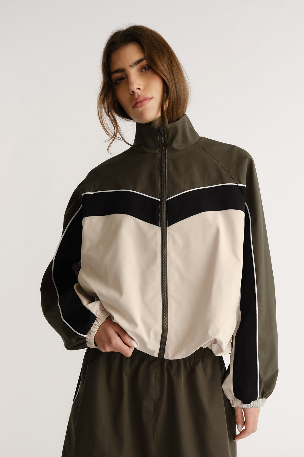 Woman wearing oversized high-neck jacket with contrast panel and zip closure posing with hand in pocket
