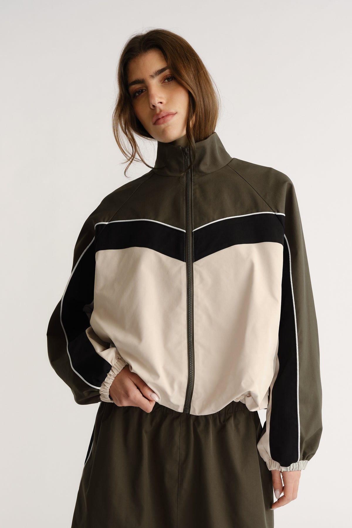 Woman wearing oversized high-neck jacket with contrast panel and zip closure posing with hand in pocket