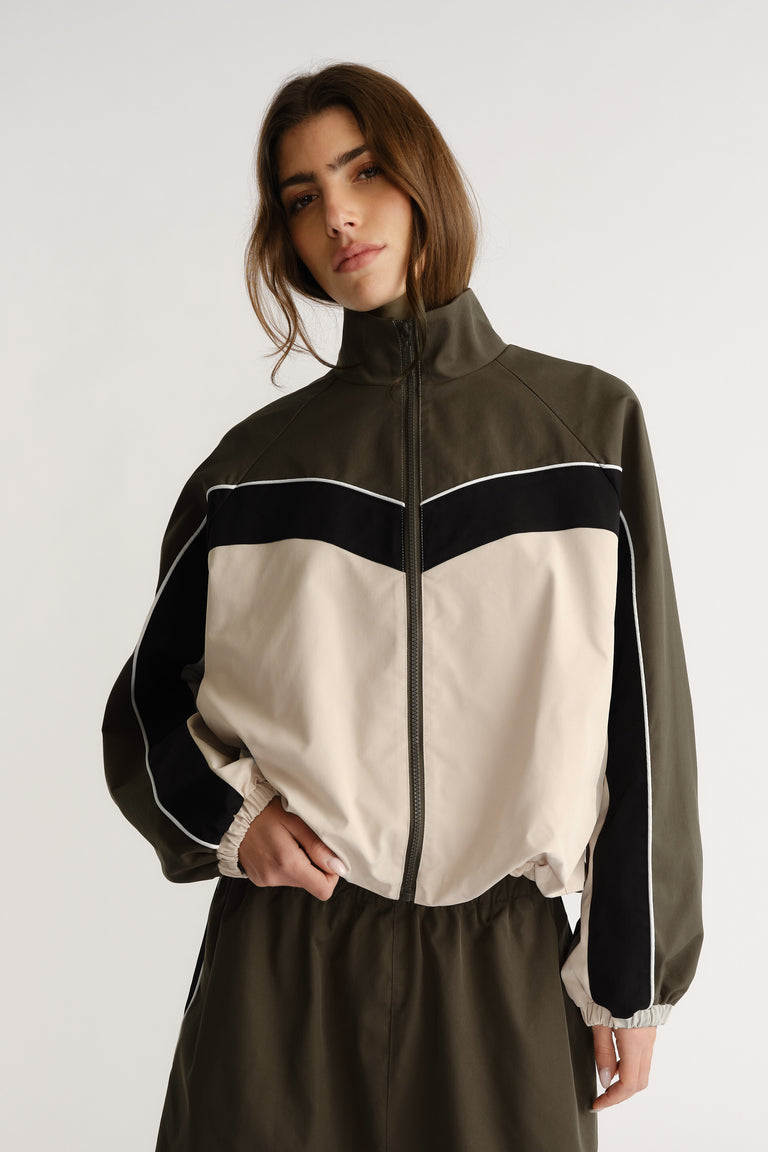 Woman wearing oversized high-neck jacket with contrast panel and zip closure posing with hand in pocket