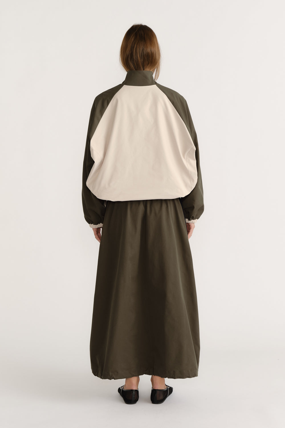 Rear view of woman wearing oversized contrast panel windbreaker with cuffed sleeves and a long olive skirt