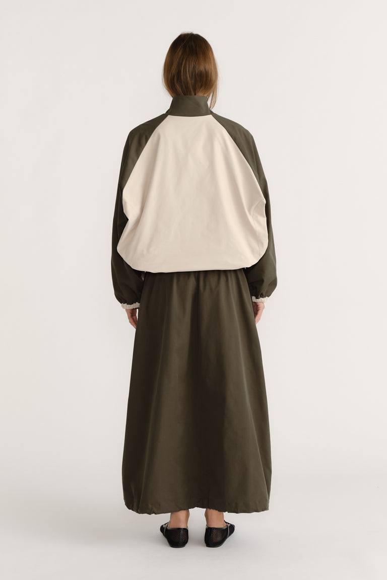 Rear view of woman wearing oversized contrast panel windbreaker with cuffed sleeves and a long olive skirt