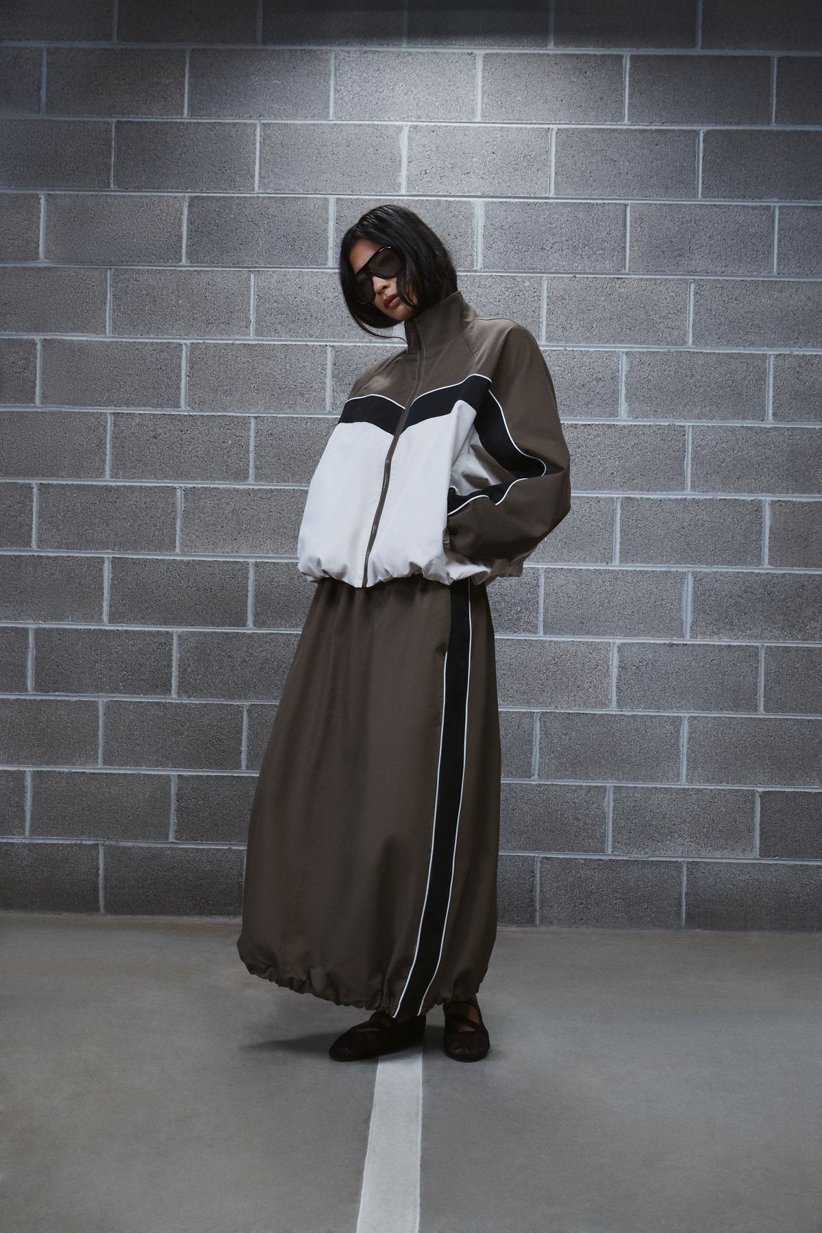Woman wearing a brown ankle length cocoon skirt with contrast side panels and a matching panelled jacket