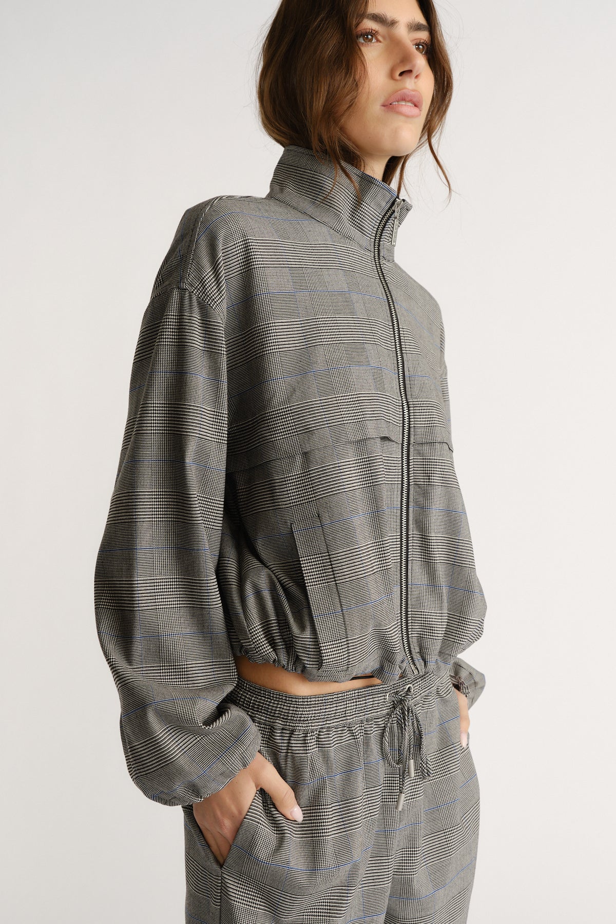 Side view of woman wearing a gray check jacket with a zip front and matching elastic waist pants.