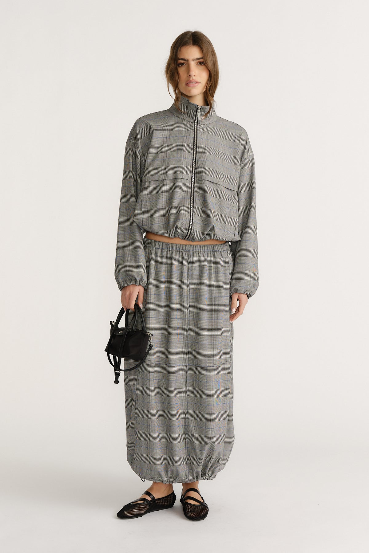 Woman wearing a gray check cocoon skirt with elastic waistband paired with matching zip-up jacket and black flats.