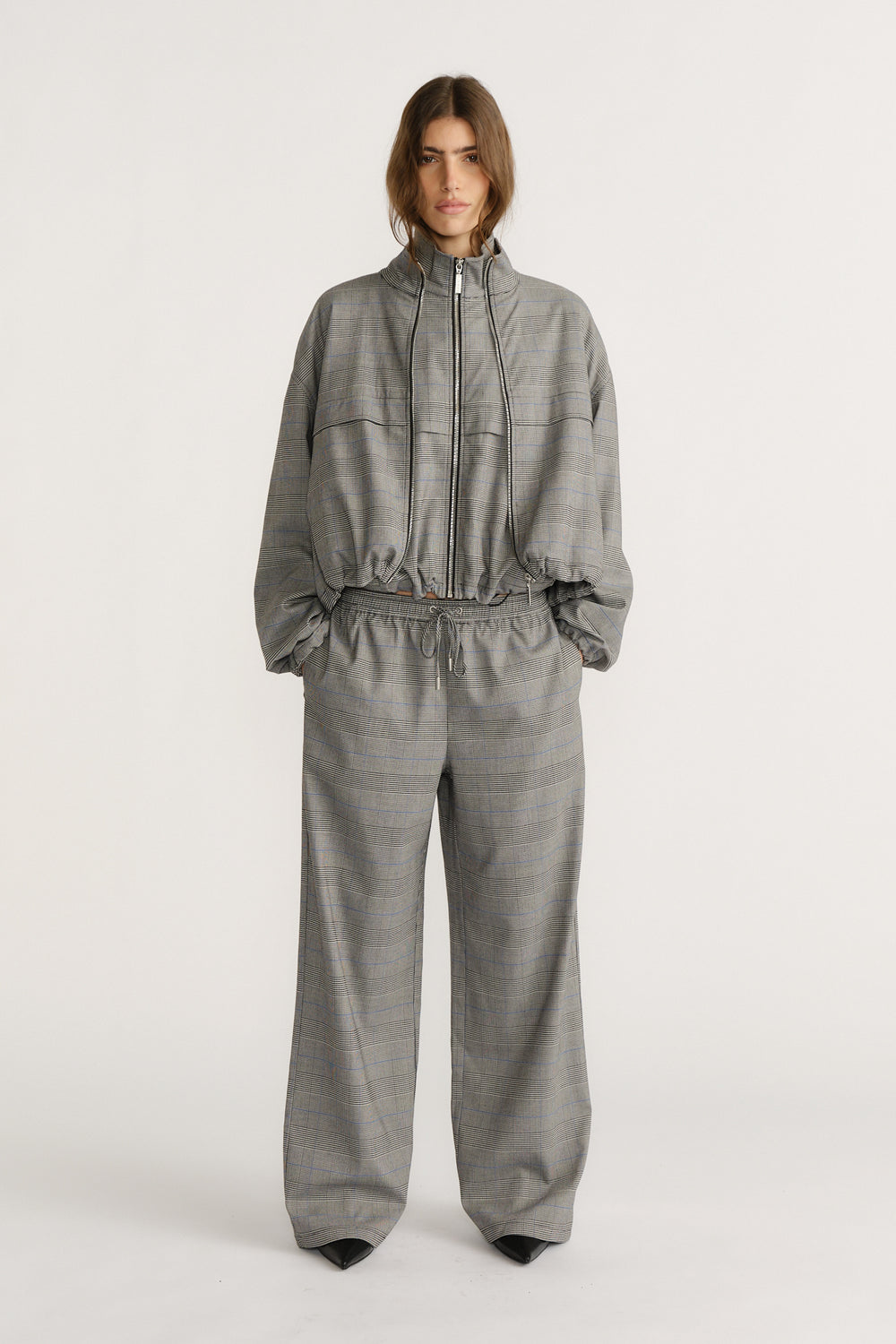 Woman wearing relaxed grey check pants with a matching zip-front jacket, styled for effortless everyday elegance.