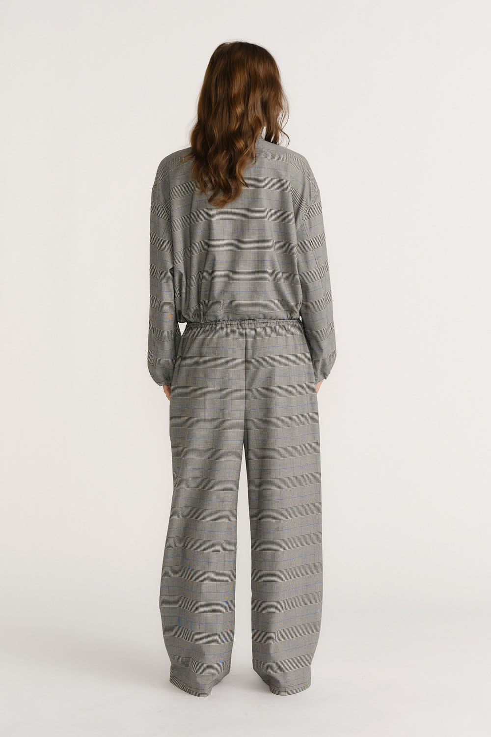 Back view of woman wearing relaxed fit check pants and matching loose top in a soft grey plaid pattern.