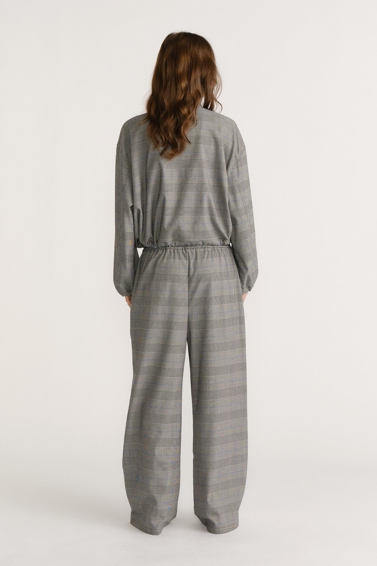 Back view of woman wearing relaxed fit check pants and matching loose top in a soft grey plaid pattern.