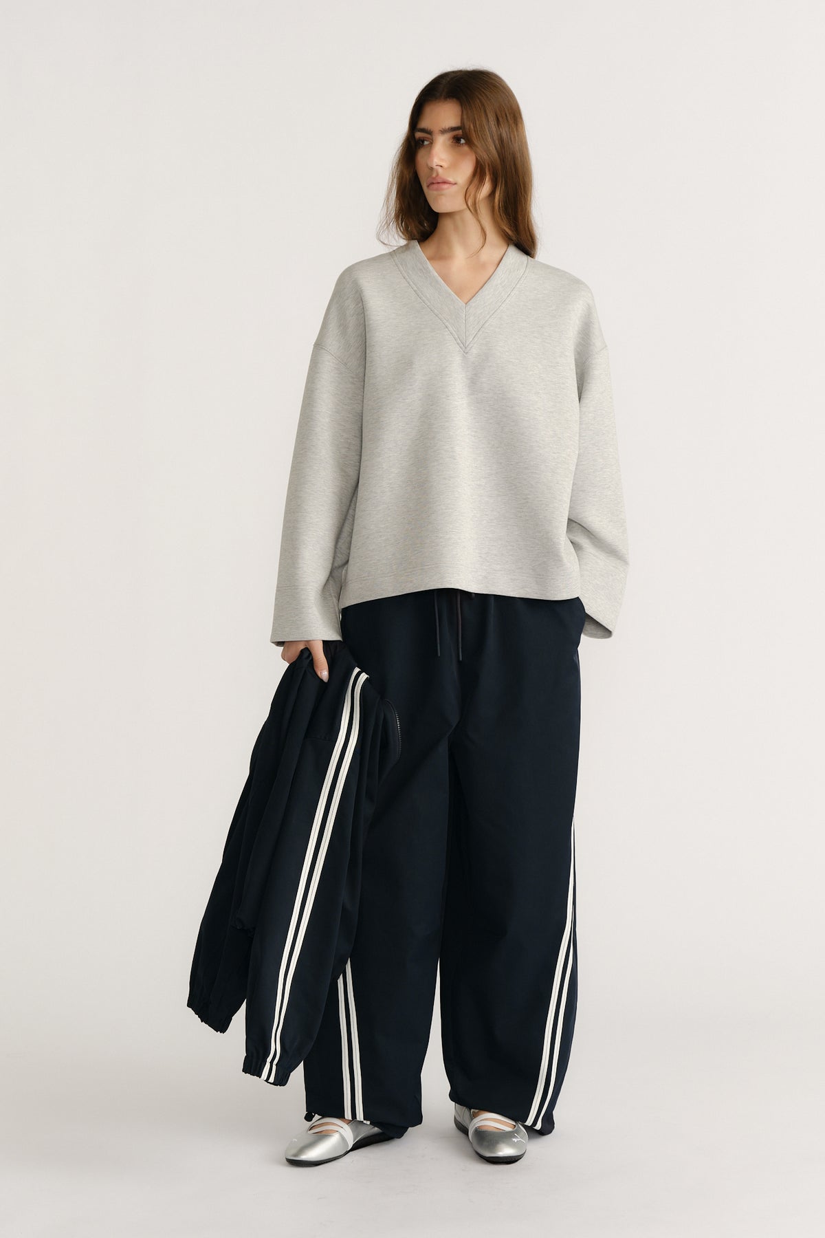 Woman wearing relaxed light grey V-neck neoprene sweat with drop shoulders paired with wide black pants with white stripes