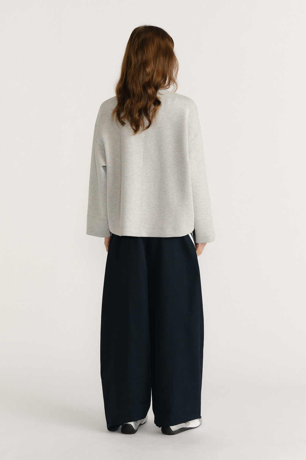 Woman wearing relaxed light grey neoprene V-neck sweat paired with loose wide-leg black pants viewed from behind