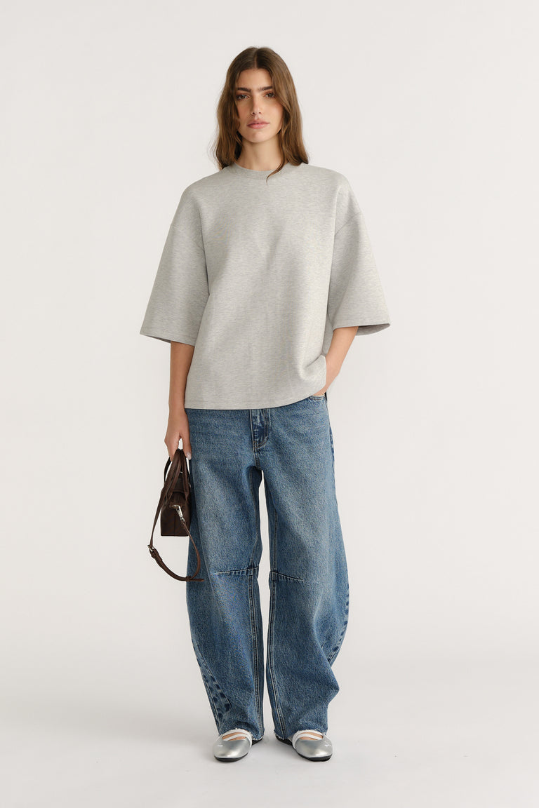 Woman wearing oversized light grey neoprene tee with drop shoulders paired with relaxed wide-leg blue jeans and silver flats