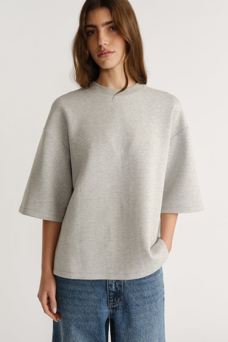 Woman wearing oversized light grey neoprene tee with half sleeves paired with relaxed blue jeans