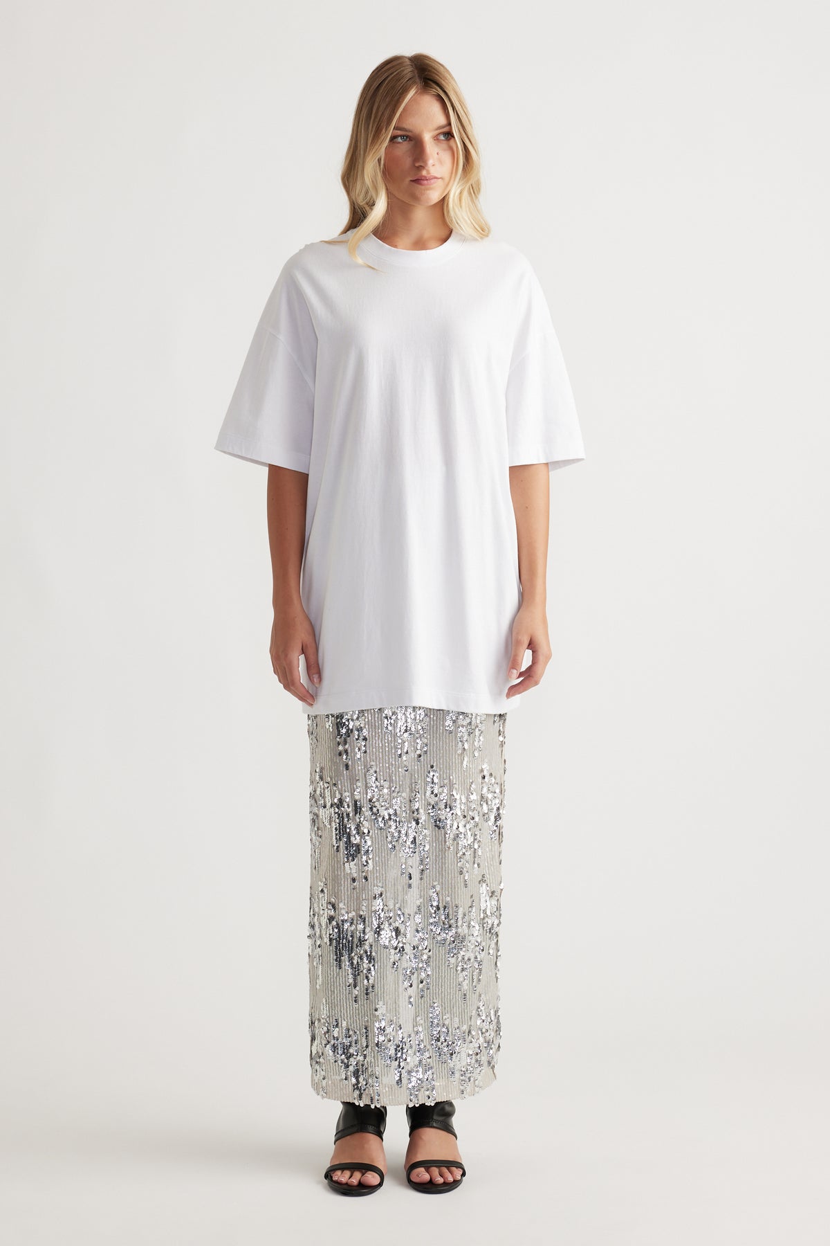Woman wearing an oversized white tee paired with a silver sequin maxi skirt and black open-toe heels