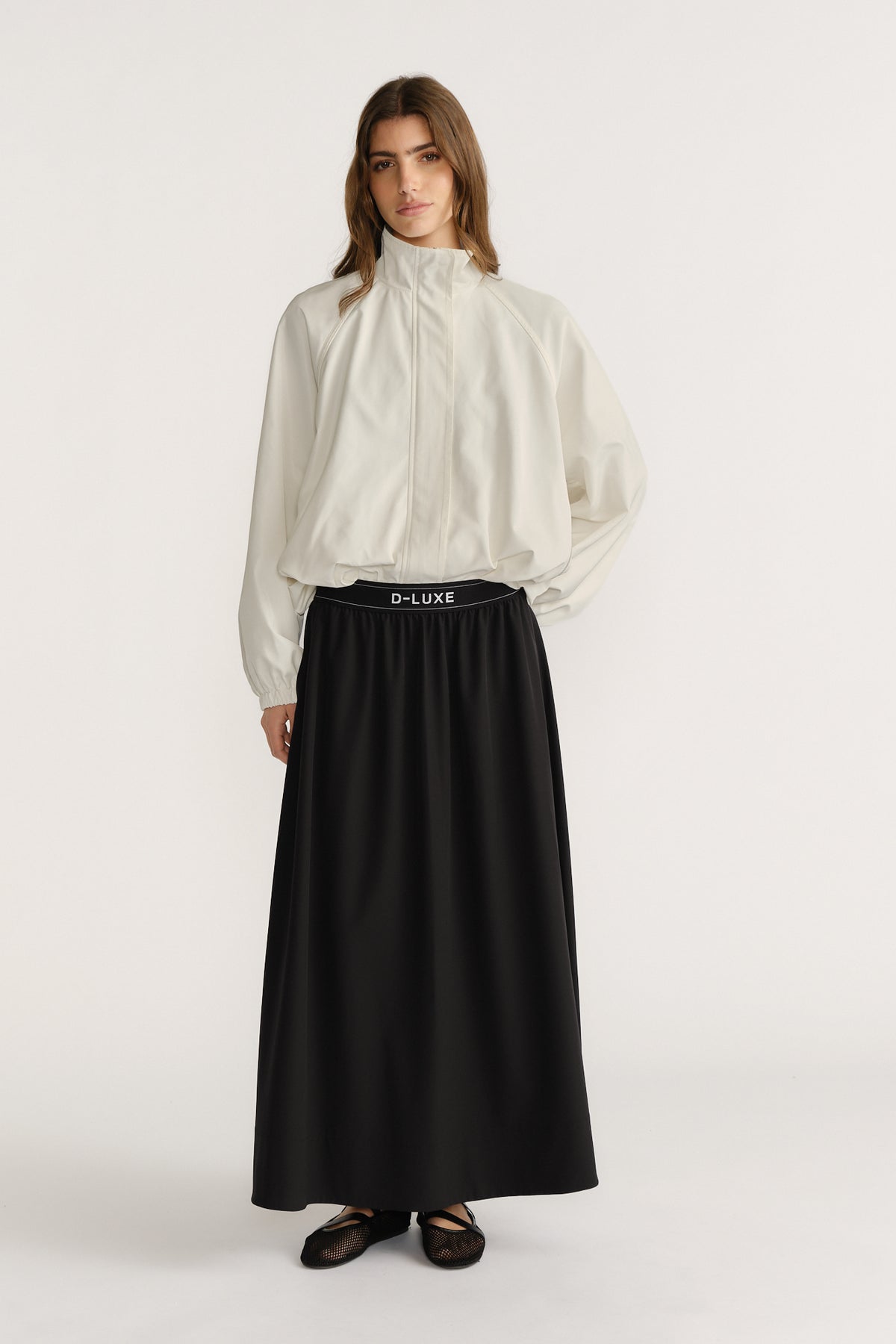 Woman wearing a high-rise black pull-on ankle-length skirt paired with a loose white zip-up jacket and flats