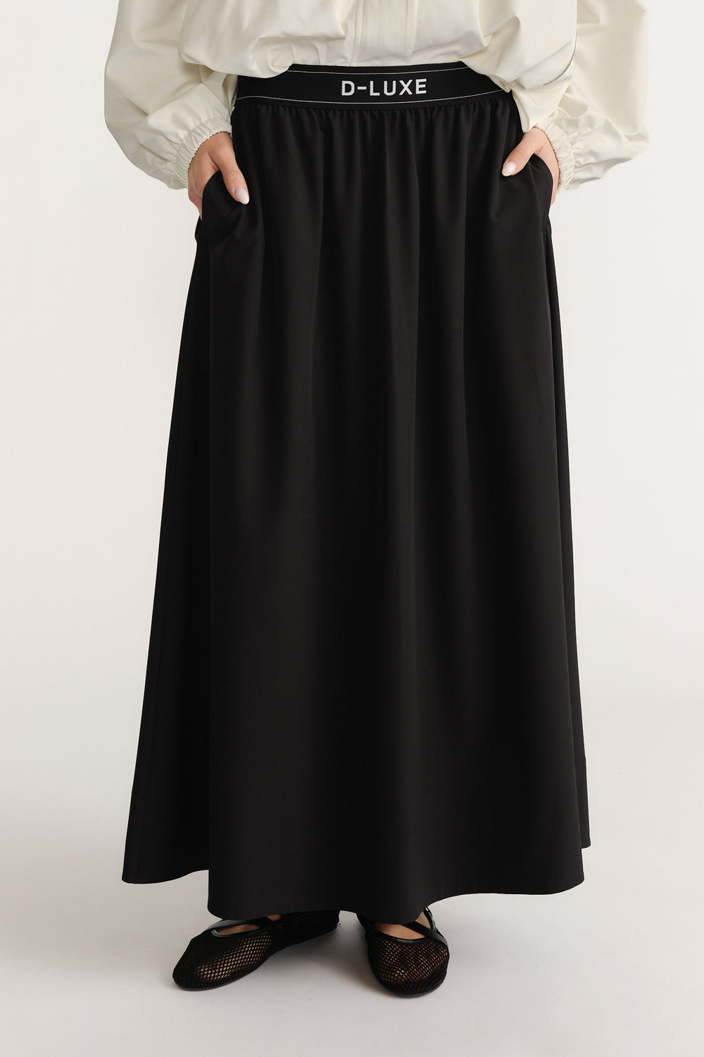 Woman wearing a black ankle-length pull-on skirt with elastic waistband and side pockets paired with black mesh flats
