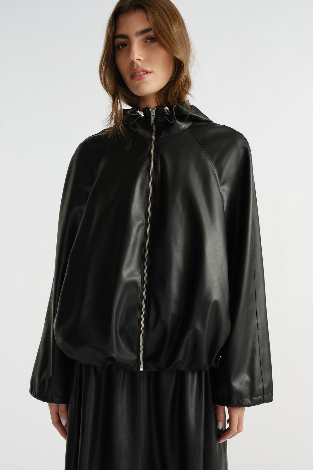 Woman wearing a black faux leather bomber jacket with a drawstring hood and relaxed fit, styled effortlessly for everyday wear