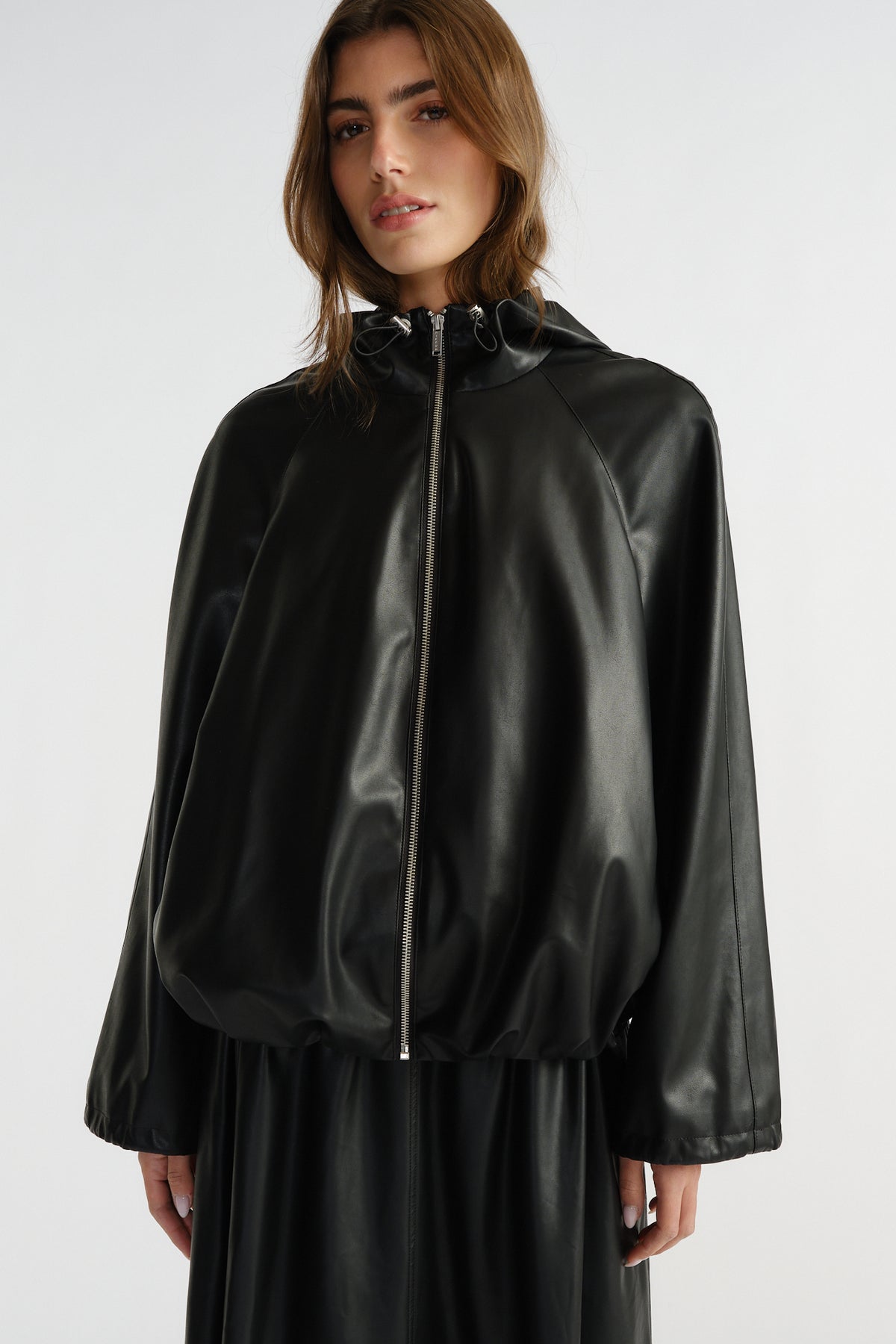 Woman wearing a black faux leather bomber jacket with a drawstring hood and relaxed fit, styled effortlessly for everyday wear