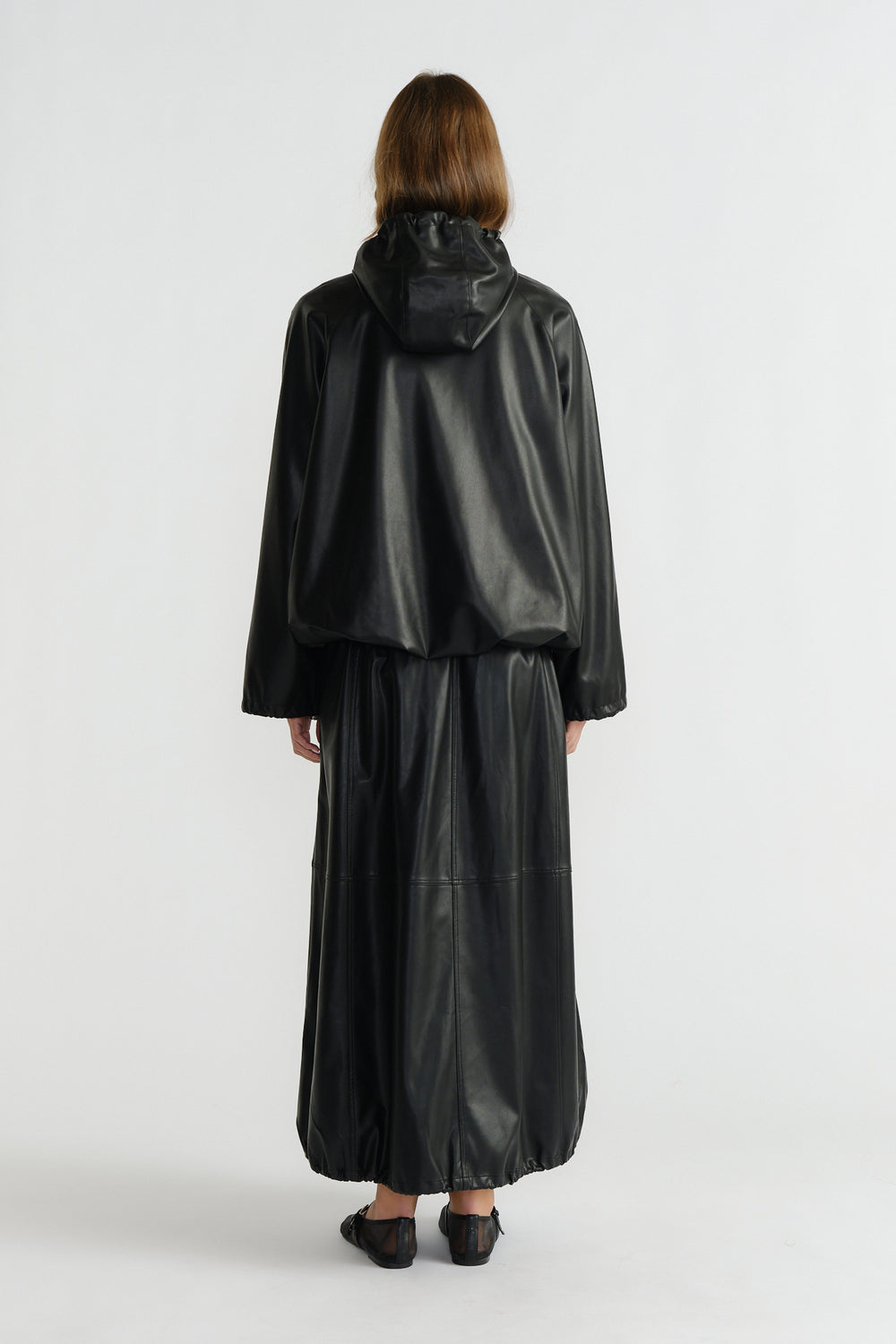 Back view of woman wearing a relaxed black faux leather bomber jacket with a hood and matching wide-leg pants