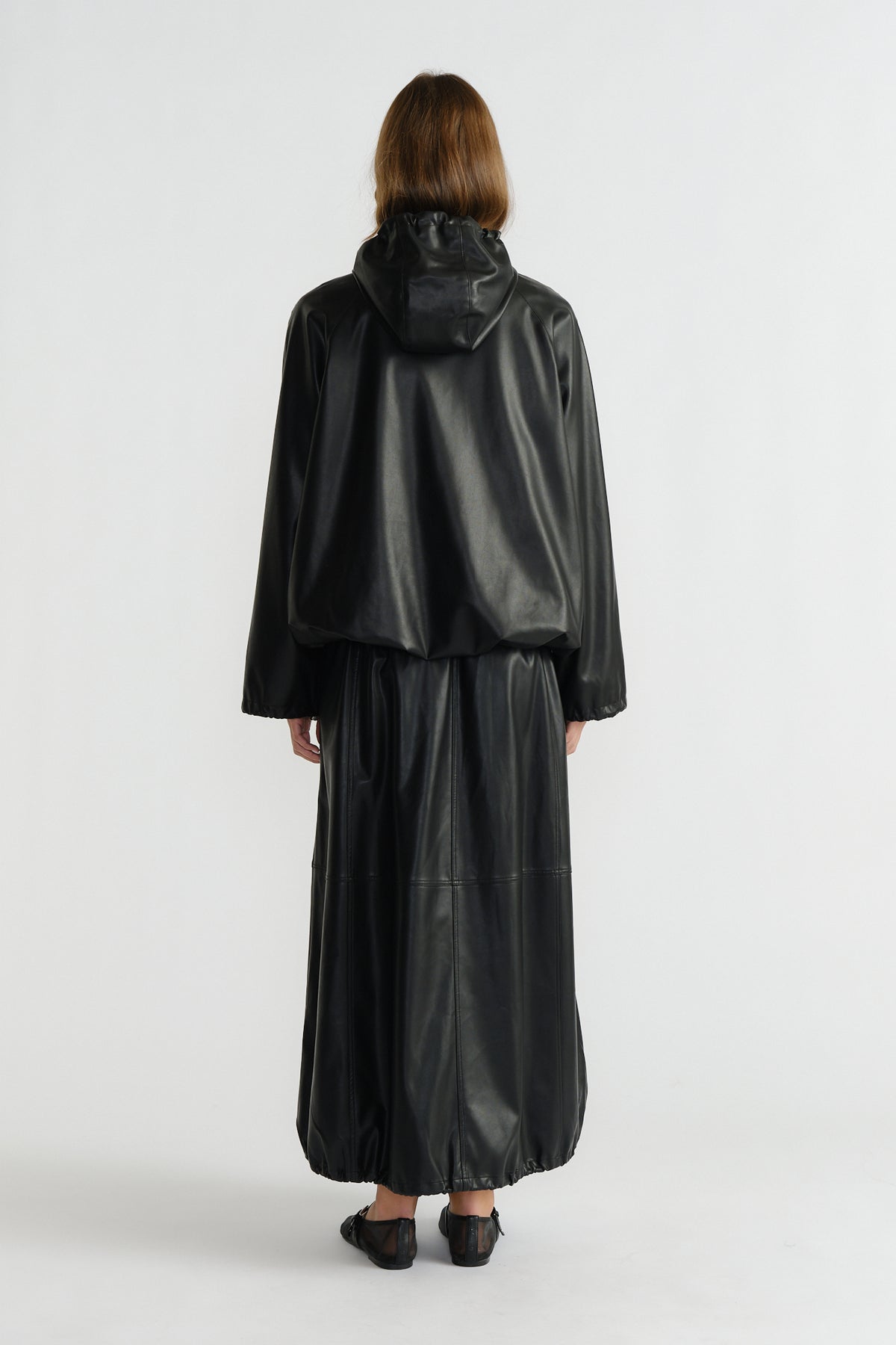 Back view of woman wearing a relaxed black faux leather bomber jacket with a hood and matching wide-leg pants