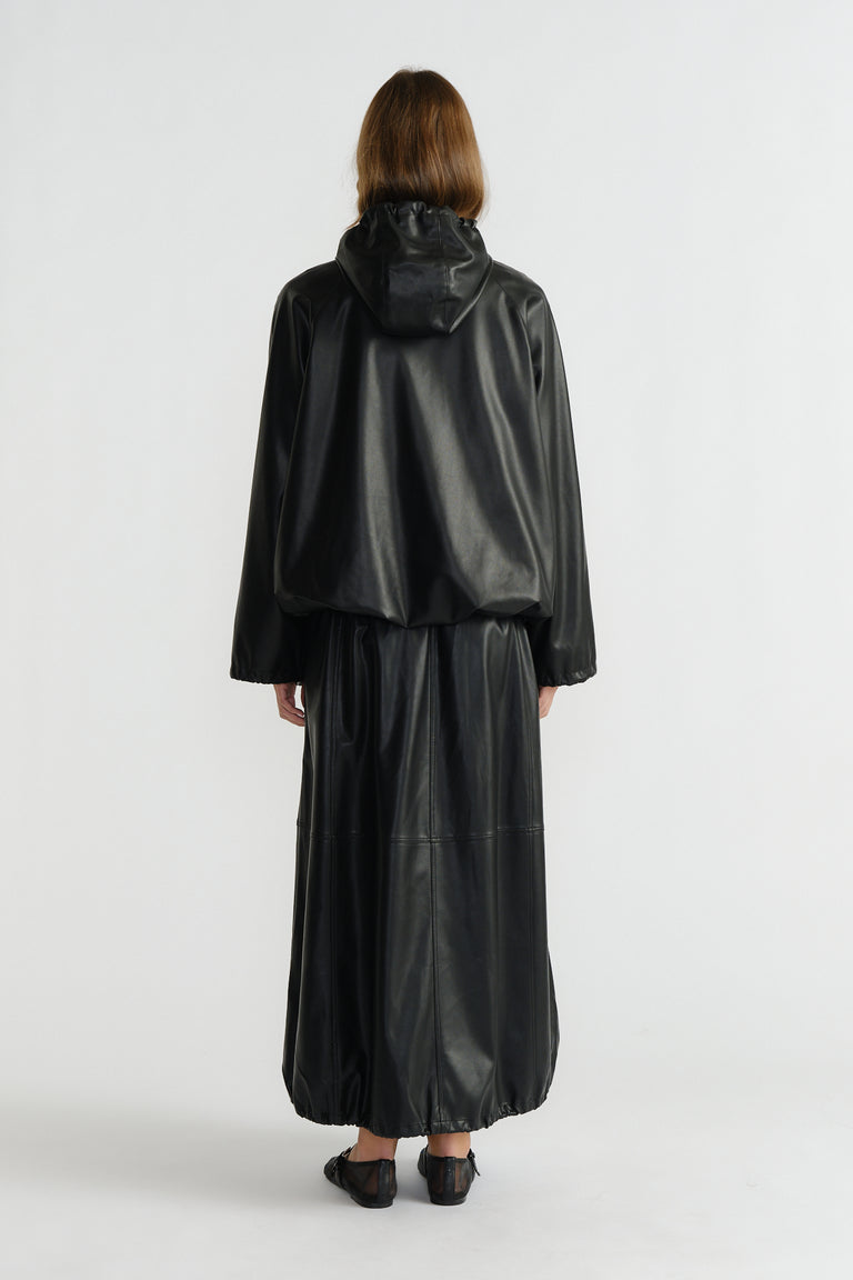 Back view of woman wearing a relaxed black faux leather bomber jacket with a hood and matching wide-leg pants