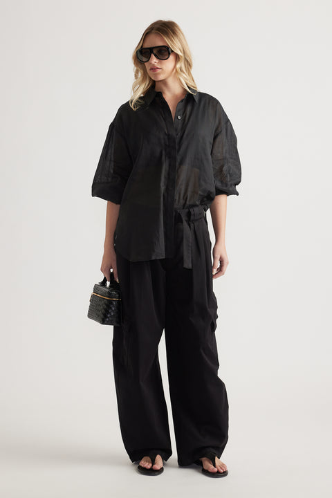Woman wearing a black oversized button through shirt with wide leg pants and sunglasses