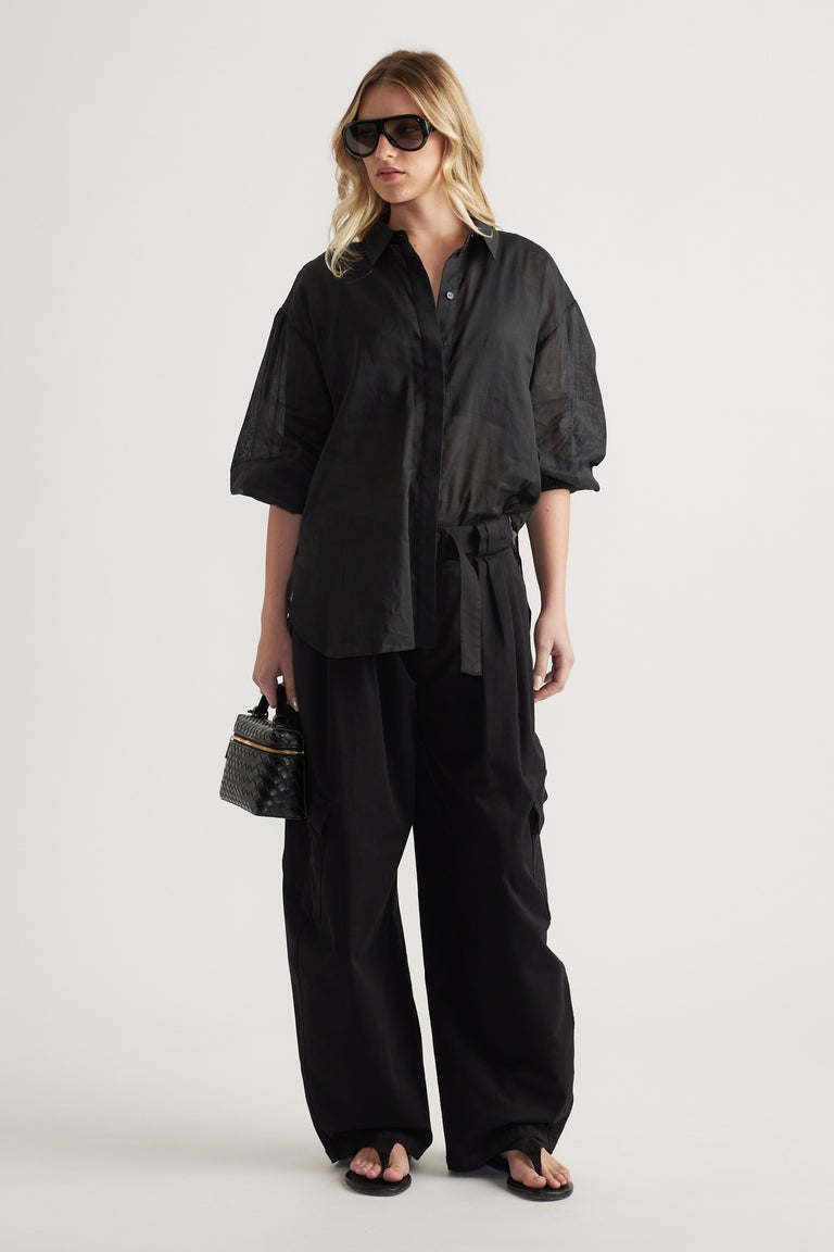 Woman wearing a black oversized button through shirt with wide leg pants and sunglasses