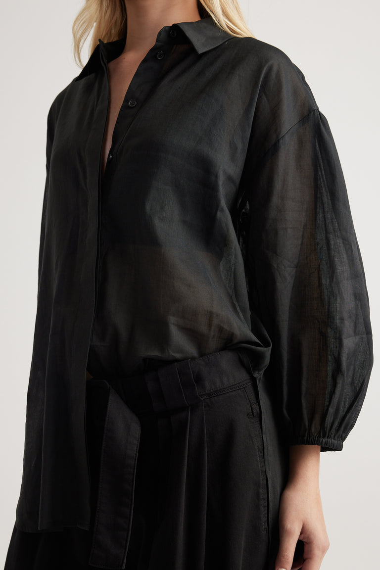 Woman wearing a black oversized sheer shirt with a collared neckline and long relaxed sleeves