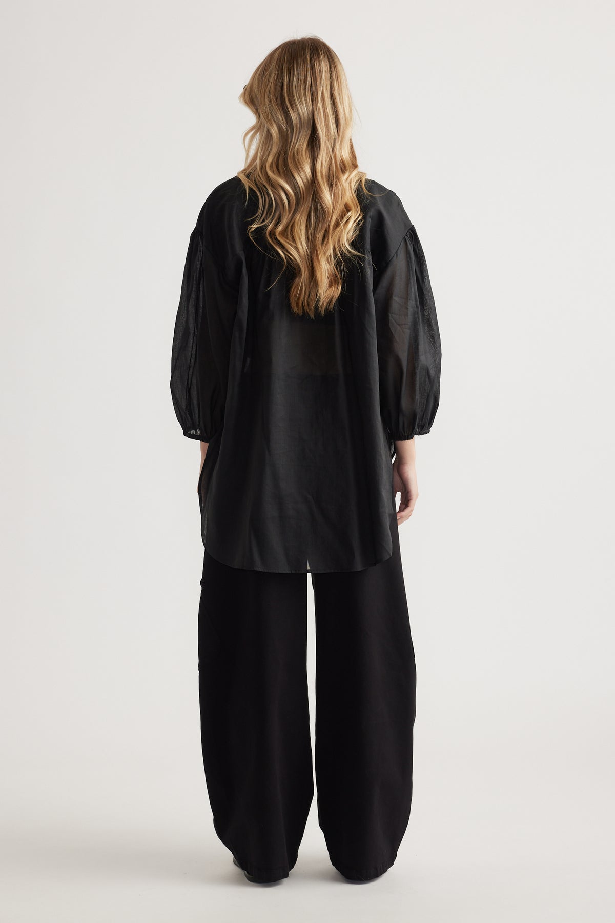 Woman viewed from behind wearing a black oversized shirt with long sleeves and wide leg pants