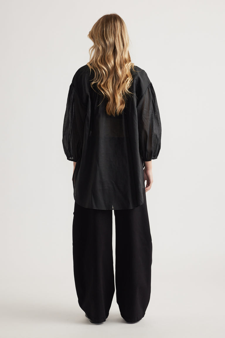 Woman viewed from behind wearing a black oversized shirt with long sleeves and wide leg pants