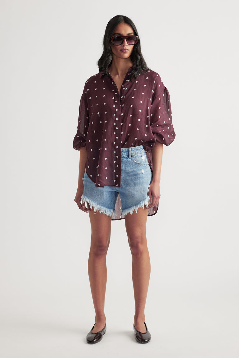 Woman wearing high rise distressed denim shorts with a burgundy printed shirt and black flats