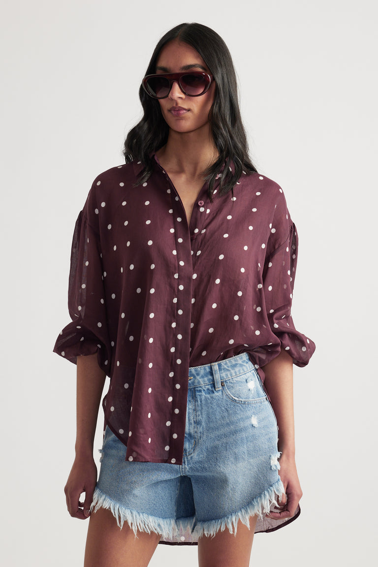Woman wearing a burgundy polka dot button through shirt with denim shorts and sunglasses