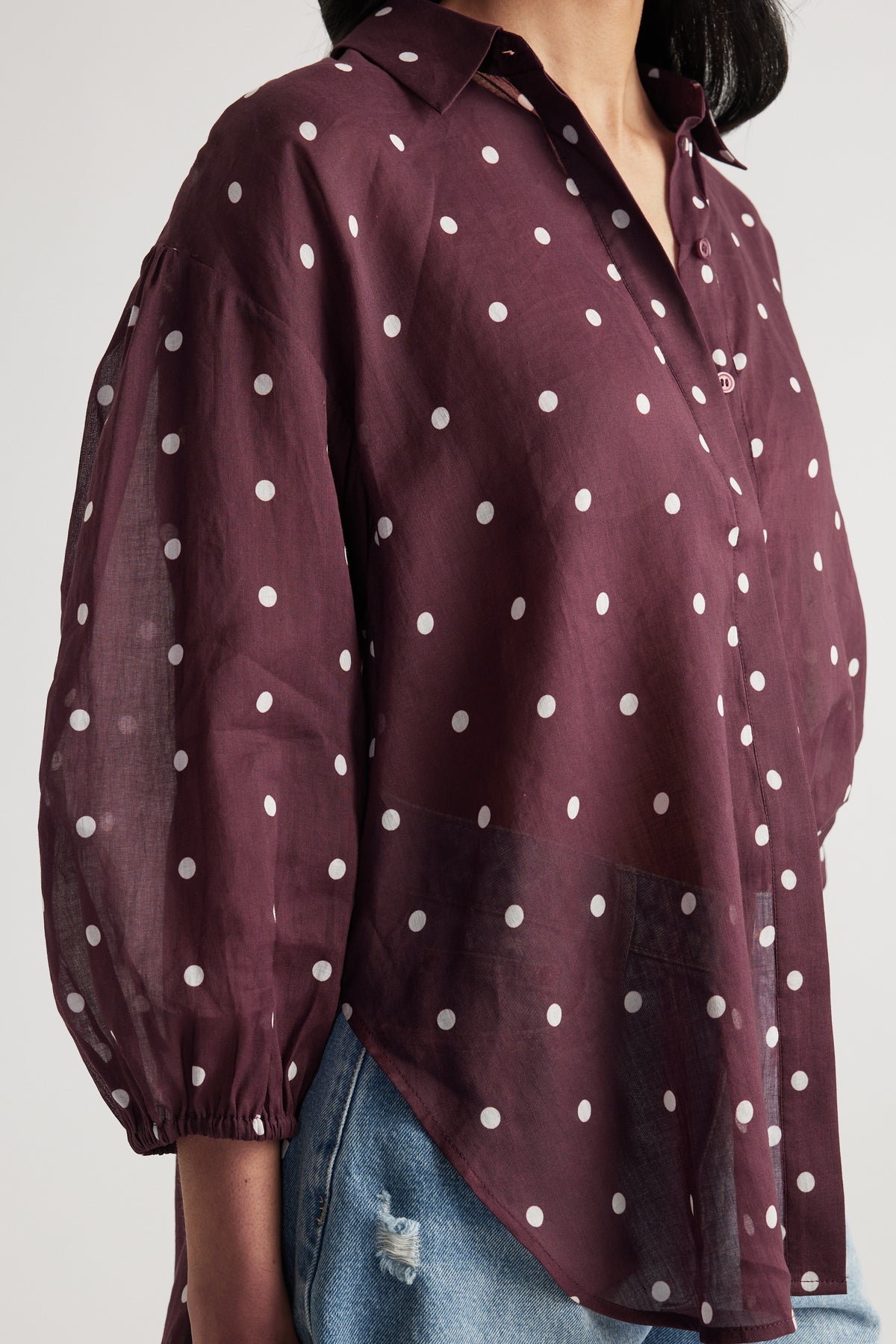 Woman wearing a burgundy sheer polka dot button through shirt with jeans