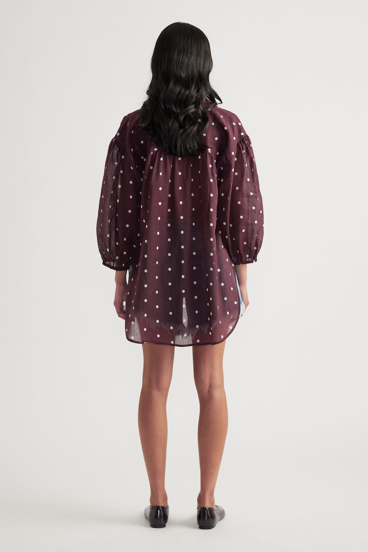 Woman seen from behind wearing a burgundy polka dot oversized shirt with long sleeves