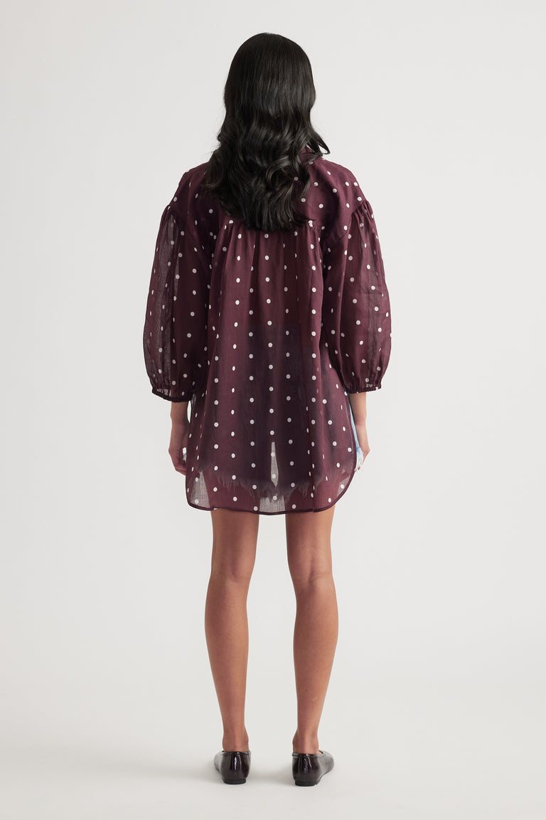 Woman seen from behind wearing a burgundy polka dot oversized shirt with long sleeves