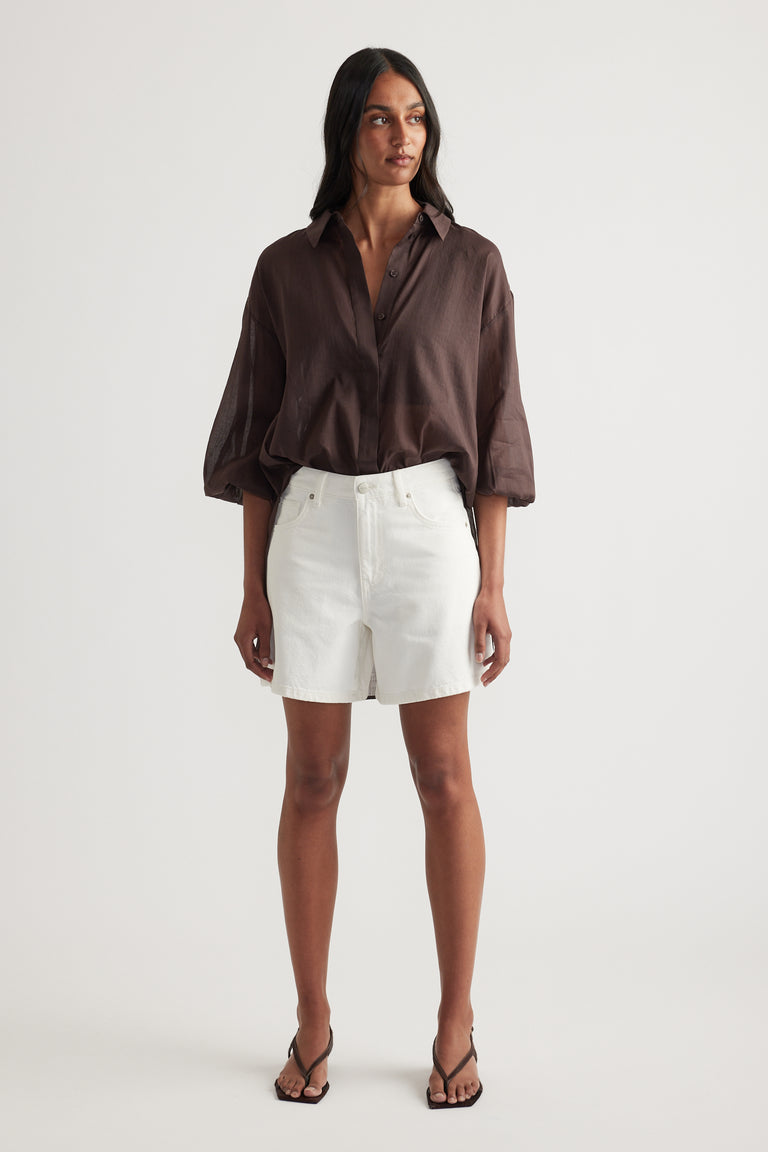Woman wearing a chocolate brown oversized shirt with white denim shorts and black strappy sandals