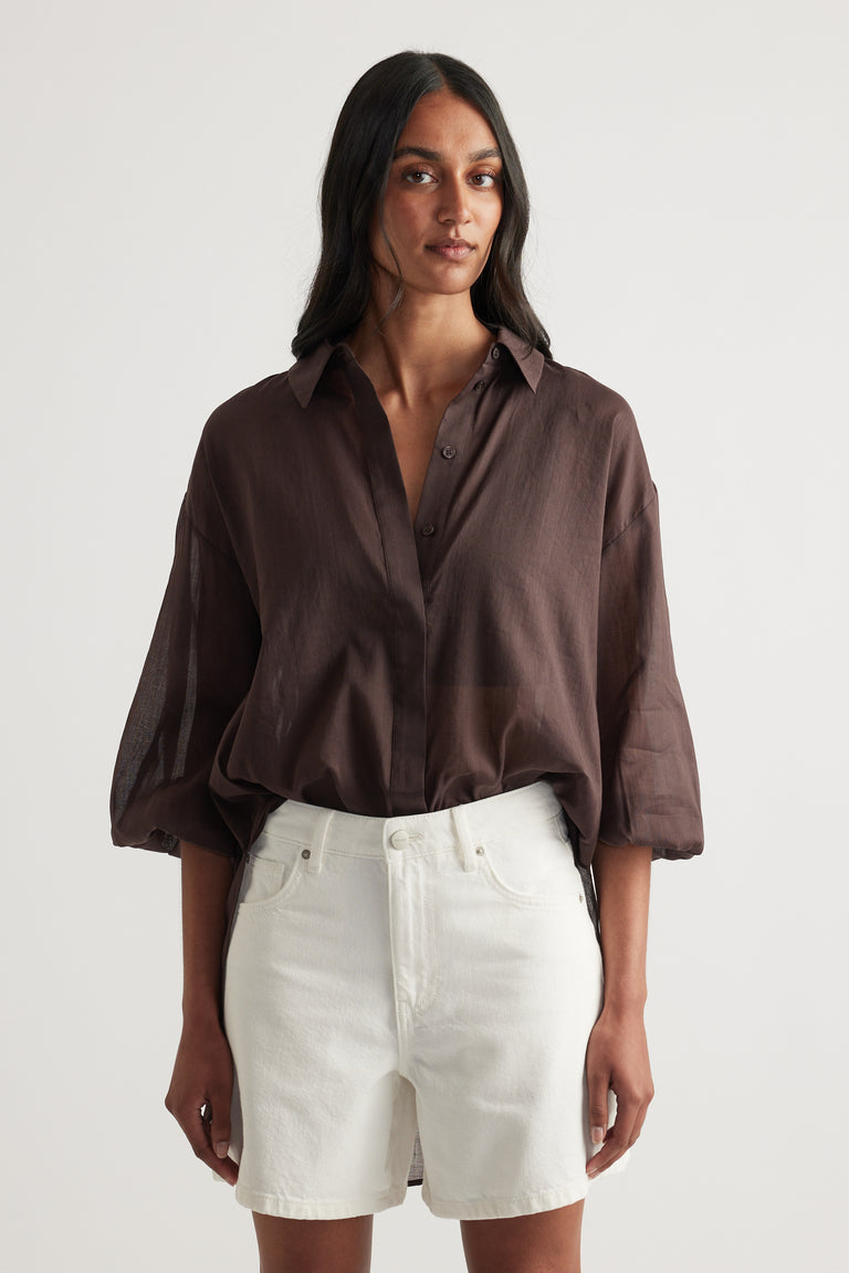 Woman wearing a relaxed brown collared shirt with long sleeves and white shorts