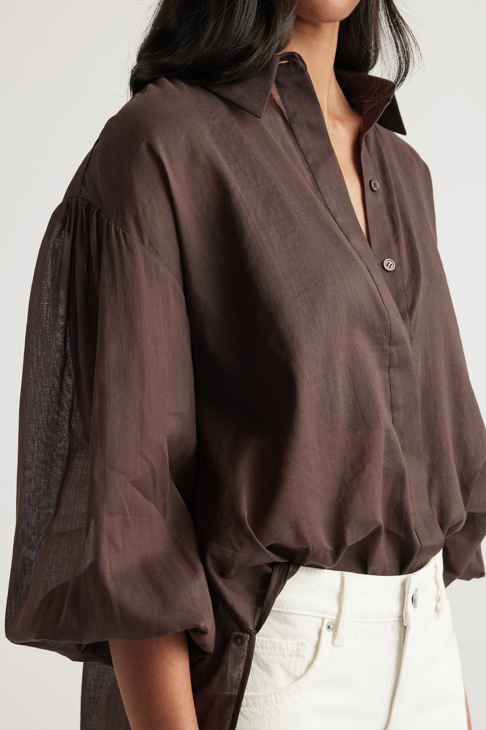 Woman wearing a brown oversized collared shirt with long sleeves and white jeans