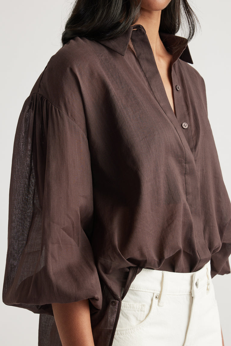 Woman wearing a brown oversized collared shirt with long sleeves and white jeans