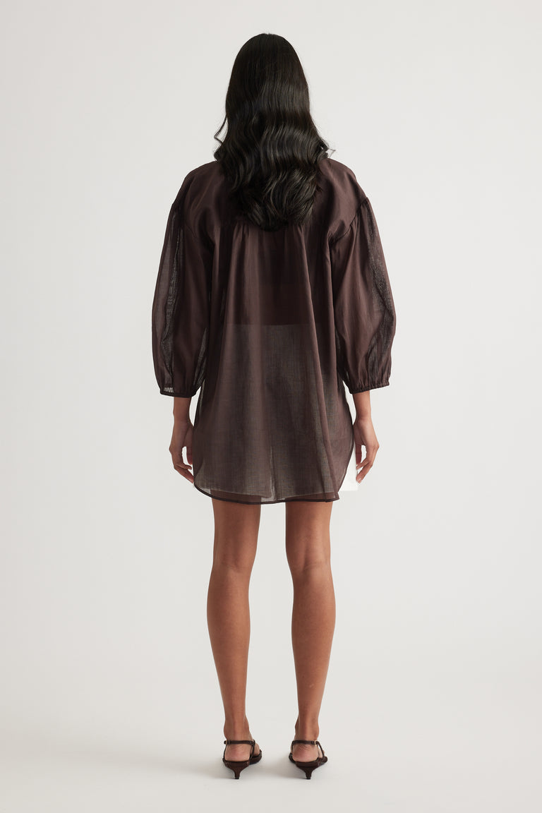 Back view of a woman wearing a dark brown oversized shirt dress with long sleeves and black heels