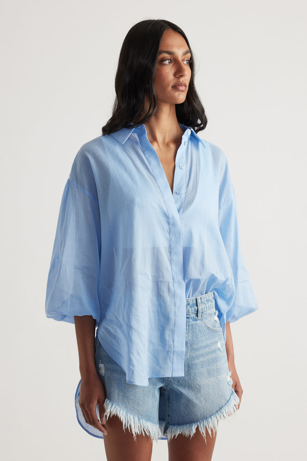 Woman wearing a light blue oversized collared shirt with frayed denim shorts